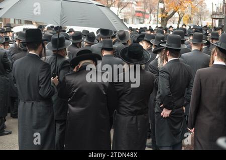 Orthodoxe jüdische Männer in schwarz gekleideter Kleidung nehmen an einer Beerdigung eines chassidischen Rabbiners Teil und hören sich eine Trauerfeier an. In Brooklyn, New York. Stockfoto