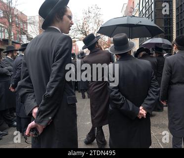 Orthodoxe jüdische Männer in schwarz gekleideter Kleidung nehmen an einer Beerdigung eines chassidischen Rabbiners Teil und hören sich eine Trauerfeier an. In Brooklyn, New York. Stockfoto