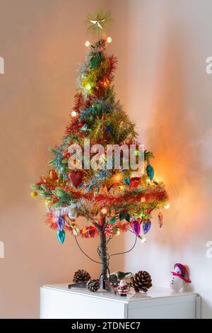 Voll dekorierter und beleuchteter Weihnachtsbaum auf weißen Möbeln in einem Hauszimmer. Stockfoto