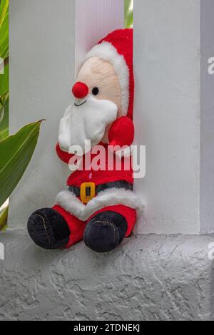 Weihnachtsmannspielzeug verkleidet, zwischen zwei Säulen auf der Veranda eines Hauses eingeklemmt, mit grünem Laub in der Nähe. Stockfoto