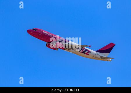 Ein Niedrigwinkelfoto eines rosafarbenen Wizz Air Flugzeugs, das in einem blauen Himmel fliegt Stockfoto