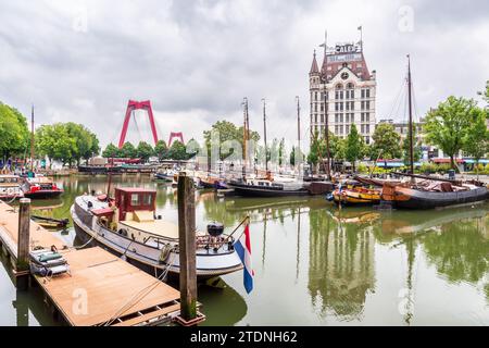 Der alte Hafen von Rotterdam mit Flussbooten, überblickt vom historischen Gebäude Witte Huis und den roten Pylonen der Willemsbrug, unter einem stürmischen Himmel. Stockfoto