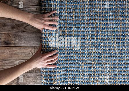 Mann, der Hand gewebte geometrische Denim-Teppich auf einem Holzboden zu Hause rollte. Stockfoto