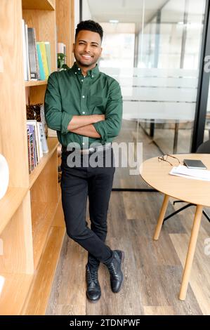 Erfolgreicher ernsthafter, selbstbewusster junger indischer Unternehmer Geschäftsmann in formeller Kleidung stehend mit überkreuzten Armen im modernen Büro, Blick in die Kamera, in voller Länge Stockfoto