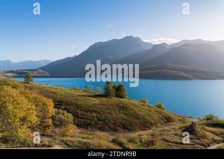 Mont-Cenis (Moncenisio) See und Berge, blauer Himmel und sanftes Licht, Ufer mit Bäumen im Herbst, Damm und klares Wasser Stockfoto