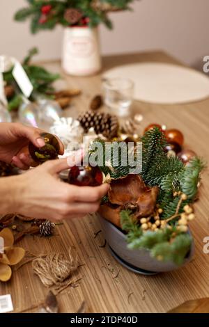 Weibliche Hände kreieren handgefertigte Weihnachtsdekoration mit Tannenzweigen und getrockneten Blumen Stockfoto