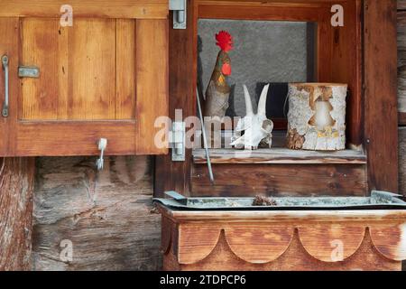 Holzhaus Mit Offenen Fensterläden. Auf den Sims Ein hölzerner Gockel, ein Tierschädel und Eine Kerze. Albines, Leuk, Wallis, Schweiz Stockfoto