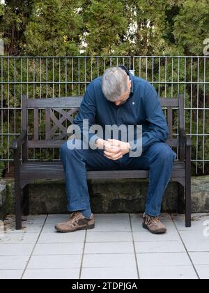Mann mit grauen Haaren und Vollbart, 50-59 Jahre alt, sitzt auf einer Bank auf der Terrasse, hängt seinen Kopf, nachdenklich, traurig Stockfoto