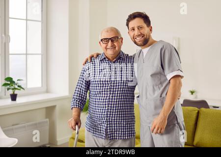 Junger Krankenpfleger, der einem älteren Patienten hilft, mit seinen Krücken zu gehen. Stockfoto