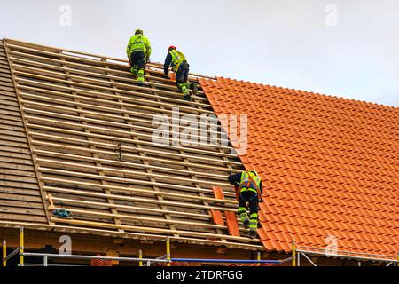 Drei Dachdecker in Schutzkleidung, die neue Tonziegel und neue Tonziegelschicht installieren Stockfoto