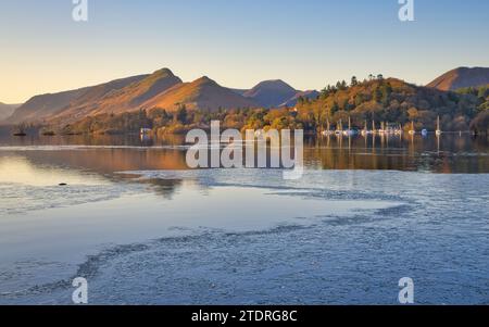 Die ersten Sonnenstrahlen des Winters erleuchten die Hänge der Catbells, die Bäume in der Brandelhow und die Boote im Yachthafen, während noch Eis über dem See liegt Stockfoto