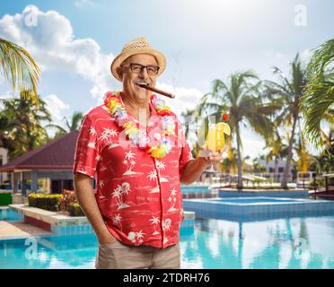 Reifer männlicher Tourist mit einem Cocktail, der eine Zigarre am Pool raucht Stockfoto