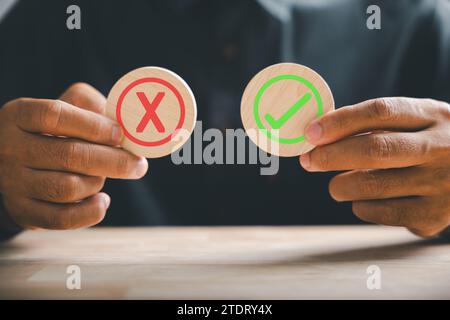 Holzwürfel in der Hand zeigen ein grünes Häkchen und ein rotes Kreuz – symbolisch für Ja oder Nein Steht für wahr Stockfoto