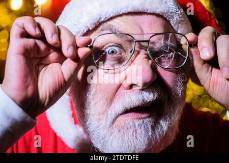 Weihnachtszeit. Weihnachtsmann mit kaputter Brille. Bärtiger Mann im Weihnachtsmannkostüm mit kaputter Herrenbrille. Weihnachtsmann, der durch ein gebrochenes Auge schaut Stockfoto