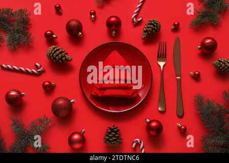 Festliche Tischdekoration mit gefalteter Serviette und Weihnachtsdekoration auf rotem Hintergrund Stockfoto