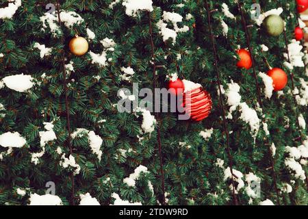 Silvester im Hintergrund. Die roten Silvester-Spielzeugbälle hängen an grüner dekorativer Fichte mit natürlichem Schnee im Freien Stockfoto