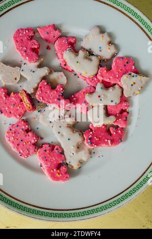 Hoher Winkel von Frosted Circus Animal Cookie Pink und White Streused Animal Cracker auf weißer Platte, goldener Hintergrund Stockfoto