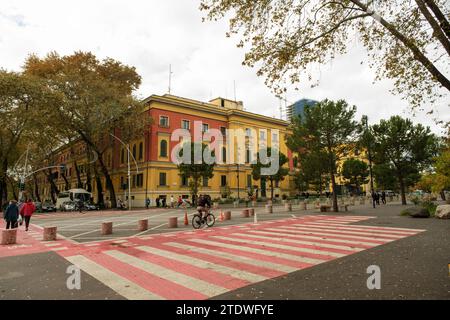 Tirana, Albanien - 29. November 2023: Ein Foto, das das Gebäude des Finanzministeriums, eine Fußgängerüberfahrt und Menschen, die in Tira spazieren und Radfahren Stockfoto