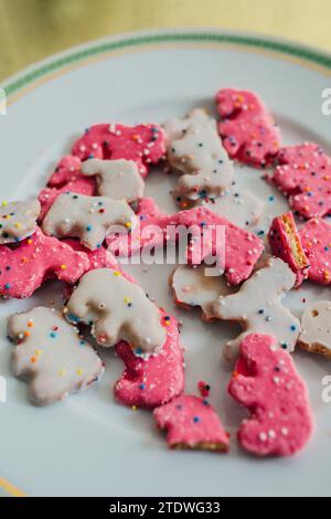 Hoher Winkel von Frosted Circus Animal Cookie Pink und White Streused Animal Cracker auf weißer Platte, goldener Hintergrund Stockfoto