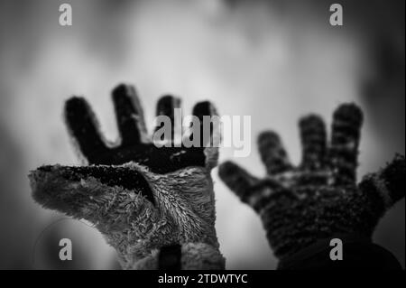 Ein Paar unpassender Handschuhe an einem Kind, das über einem weißen Schneehintergrund gehalten wird Stockfoto