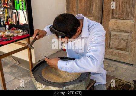 27. JUNI 2023, BUCHARA, USBEKISTAN: Der Meister, der die Metallarbeiten für den Verkauf als Souvenir macht Stockfoto