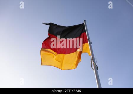 Deutsche Flagge auf einem Fahnenmast, der im Wind gegen blauen Himmel winkt Stockfoto