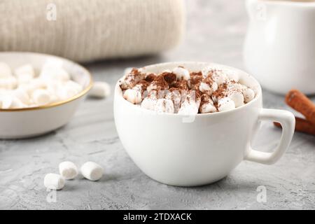 Tasse aromatische heiße Schokolade mit Marshmallows und Kakaopulver auf grauem Tisch, Nahaufnahme Stockfoto