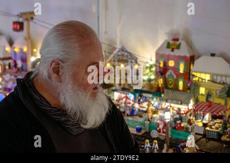 Coburg, Deutschland. Dezember 2023. Horst Gründel schaut sich seinen kleinen Weihnachtsmarkt an. Rund 20 Meter vom Coburger Marktplatz aus fliegt der ausgebildete Sozialarbeiter und jetzige Rentner Horst Gründel eine einzigartige, detailreiche Winterwelt. In einem Raum in seiner Wohnung befindet sich ein kleiner Weihnachtsmarkt mit einer Größe von etwa acht Quadratmetern. Über 30 Stände, eine Modelleisenbahn, vier Krippen, eine Gondel, ein Karussell und vieles mehr beleben die Landschaft. Gründel begann in den 1970er Jahren mit dem Bau der ersten Verkaufsstände Quelle: Pia Bayer/dpa/Alamy Live News Stockfoto