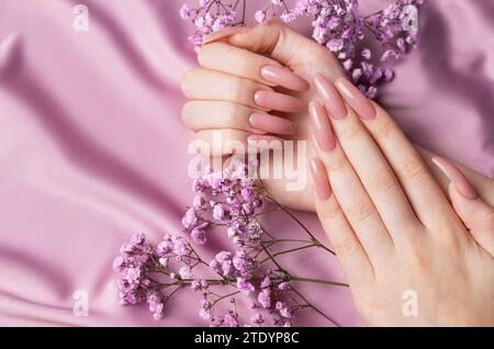 Weibliche Hände mit schöner Maniküre mit Gipsofila-Blüten auf rosa Seide Stockfoto