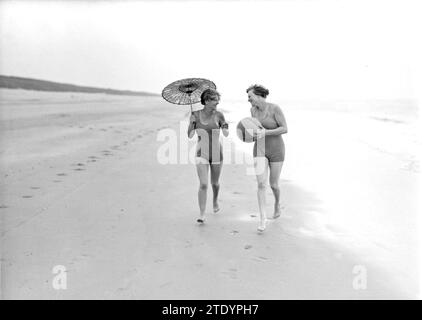 Model Eva Waldschmidt (mit Schirm) und Nell Langlais laufen entlang der Gezeitenlinie in Zandvoort CA. 1932 Stockfoto