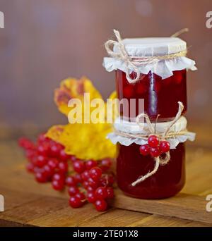 Viburnum-Konfitüre. Rote saftige Beeren von einem Viburnum mit Zucker in einem Glas auf dunklem hölzernem Hintergrund. Zum Zubereiten von Marmelade, Tee. Stockfoto