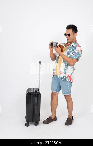 Ein fröhlicher asiatischer Mann in Sonnenbrille und Sommerkleidung macht es Spaß, während seiner Reise Fotos zu machen, und steht auf einem isolierten weißen Atelierhintergrund Stockfoto