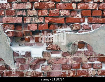 Beschädigter Putz an roter Ziegelwand im Winter Stockfoto