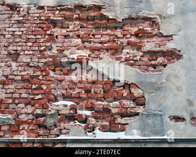 Beschädigter Putz an roter Ziegelwand im Winter Stockfoto