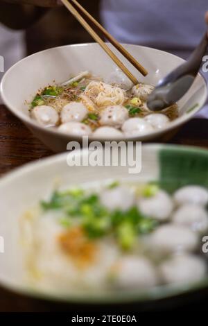 Nahaufnahme von weißer Reisnudel, klarer Suppe, Fleischbällchen mit Zutaten in einer weißen Schüssel. Stockfoto