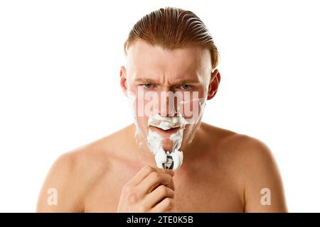 Gesichtspflege. Seriöses männliches Model, attraktiver Kerl, der seinen Bart mit Rasierer vor weißem Studio-Hintergrund rasiert. Stockfoto