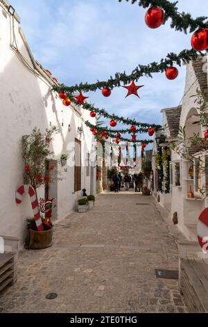 Alberobello, Italien - 2. Dezember 2023: Straße im Bezirk Rione Monti von Alberobello mit Trulli-Häusern und -Hütten und farbenfroher Weihnachtsdekoration Stockfoto