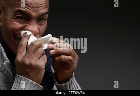 Mann, der die Erkältung und Grippe fängt Mann, der Nase bläst, nachdem er eine Erkältung mit grauem Hintergrund mit Leuten Stock Foto gefangen hat Stockfoto