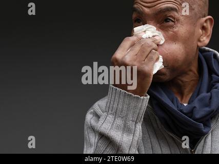 Mann, der die Erkältung und Grippe fängt Mann, der Nase bläst, nachdem er eine Erkältung mit grauem Hintergrund mit Leuten Stock Foto gefangen hat Stockfoto