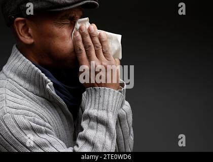 Mann, der die Erkältung und Grippe fängt Mann, der Nase bläst, nachdem er eine Erkältung mit grauem Hintergrund mit Leuten Stock Foto gefangen hat Stockfoto
