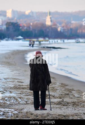 Ältere Frau mit einem Stock, die an einem verschneiten Wintertag in Polen, Europa, EU in Richtung der Kurstadt Sopot an der Ostseeküste geht Stockfoto