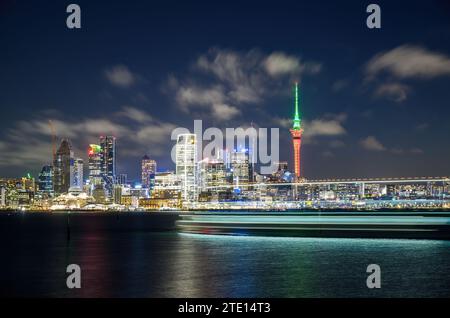 Sky Tower leuchtet in Rot und Grün zu Weihnachten. Lange Exposition mit leichten Spuren eines Bootes, das am Hafen von Waitemata vorbeifährt. Auckland. Stockfoto