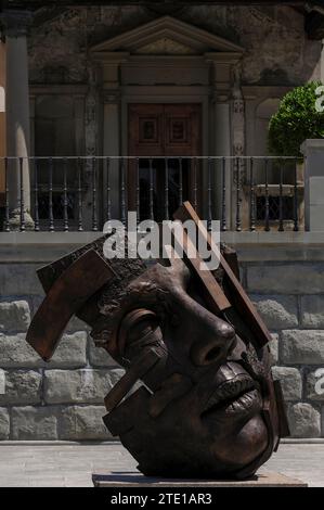 Skulptur eines riesigen menschlichen Kopfes des polnischen Künstlers Igor Mitoraj (1944–2014) auf der Piazza Mino da Fiesole, dem Hauptplatz von Fiesole, einer Stadt oberhalb von Florenz, Toskana, Italien. Im Hintergrund befindet sich der ionische Portikus der Chiesa di Santa Maria Primerana, der dieser mittelalterlichen Kirche 1801 hinzugefügt wurde. Die Fassade der Kirche stammt aus den späten 1500er Jahren Stockfoto