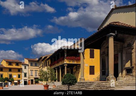 Leuchtend rote Blumen zieren die Loggia des Palazzo Pretorio oder Rathauses mit Blick auf den Hauptplatz in Fiesole, einer Stadt auf einem Hügel oberhalb von Florenz, Toskana, Italien. Rechts vom Palazzo befindet sich der ionische Portikus der Chiesa di Santa Maria Primerana, der 1801 zu dieser mittelalterlichen Kirche hinzugefügt wurde. Die Fassade der Kirche stammt aus den späten 1500er Jahren Die Via Santa Maria befindet sich zwischen dem Palazzo und der Kirche. Stockfoto