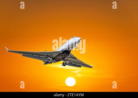 Privates Geschäftsflugzeug, das unter dem orangefarbenen Sonnenunterganghimmel fliegt Stockfoto