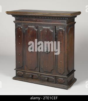 Wandschrank aus Nuthout, anonym, 1500 - 1600 Wandschrank aus Nussbaum, auf profiliertem Boden. Der Schrank hat unten eine Schublade, über der zwei Türen, alle Paneele mit abgeschrägten Ecken sind. Sowohl die Schublade als auch die Türen sind von einer ähnlich schmalen Verkleidung flankiert. Die Bedienfelder von und neben der Schublade verfügen über eine Schaltfläche „Zeichnen“. Die Türen zeigen in der Mitte Bronzeknöpfe in Form von geflügelten Cherubköpfen; im Schloss ein alter Schlüssel mit angegriffenem Griff. Das Obermaterial hat viele Profile und ragt hervor. Bologna-Holz (Pflanzenmaterial). Nussbaum (Hartholz). Bronze (Metall) Wandschrank aus Nussbaum, Stockfoto
