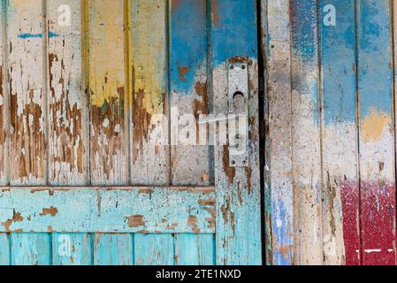 Abschnitt einer bunt bemalten alten Tür mit abblätternden Holzbrettern und silbernem Türgriff. Stockfoto