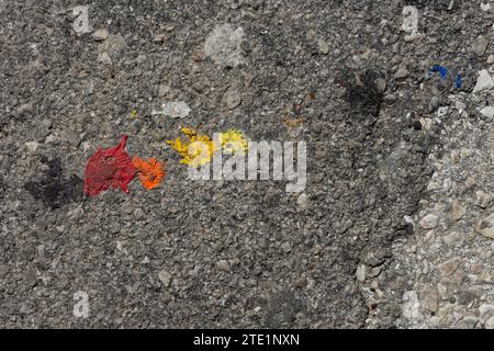Rote, gelbe, orange und blaue Farbe verschüttete in großen Tropfen auf einer gerissenen, schmutzigen Asphaltstraße. Stockfoto