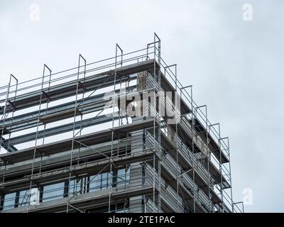 Gerüste an einer Hauswand. Die Dämmung ist mit Fassadenteilen bedeckt. Das im Bau befindliche Gebäude bietet mehrere Wohnungen im Stadtteil. Stockfoto