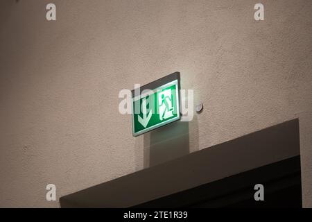 Fluchtwegschild über einer Tür an einer Wand. Das beleuchtete Notausgangssymbol ist in öffentlichen Gebäuden in Deutschland obligatorisch. Der Pfeil zeigt den Ausgang an. Stockfoto